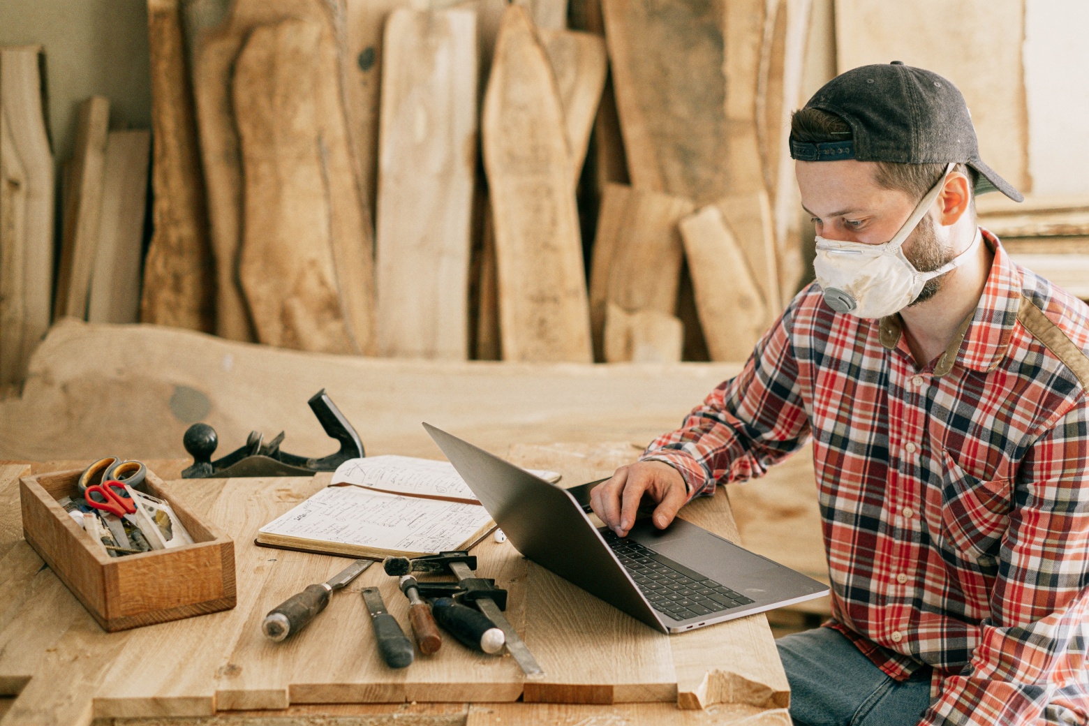 Man with mask on sitting by his laptop with engineering tools around